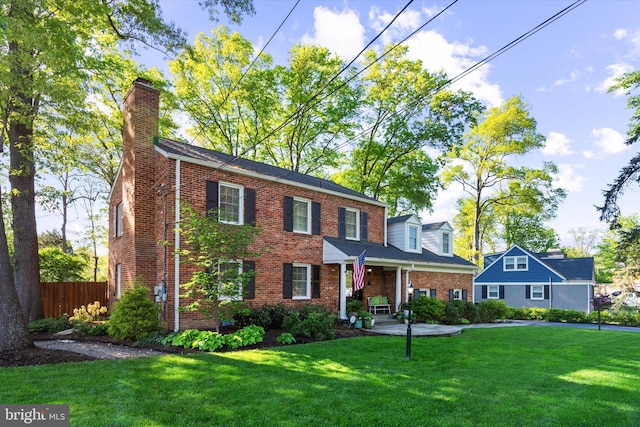 colonial-style house featuring a chimney, a front yard, fence, a porch, and brick siding