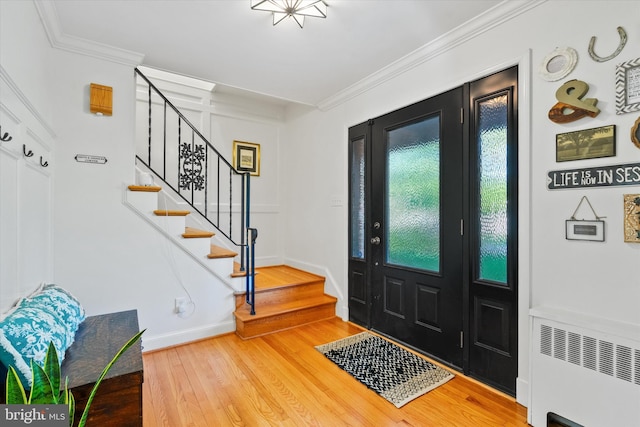foyer with radiator heating unit, wood finished floors, crown molding, and stairs