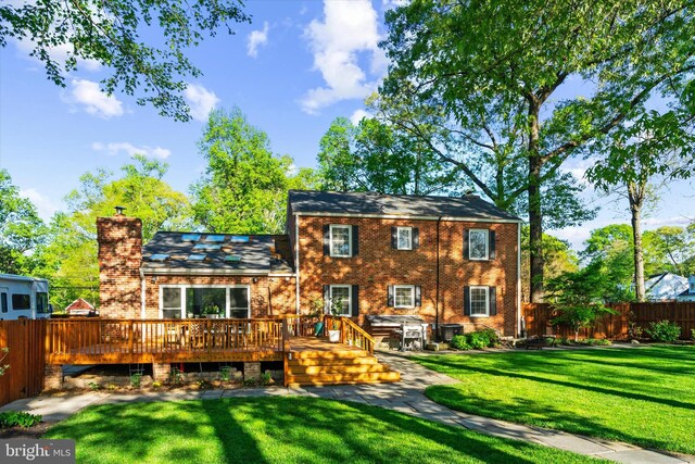 back of property featuring a chimney, a yard, brick siding, fence, and a wooden deck