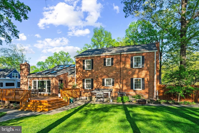 back of house featuring a lawn, a deck, fence, and brick siding