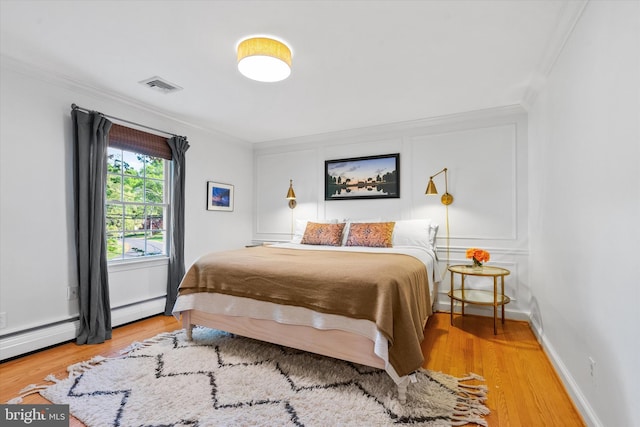 bedroom with crown molding, a baseboard heating unit, visible vents, and wood finished floors