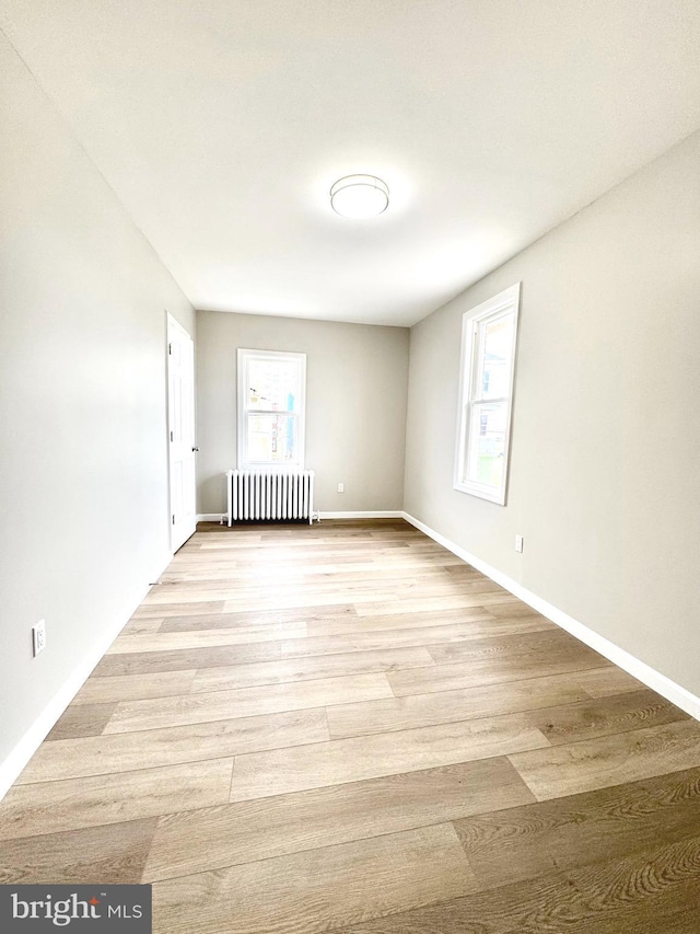 spare room with baseboards, radiator heating unit, and light wood-style floors