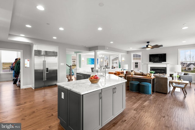 kitchen with a sink, dark wood-type flooring, built in fridge, a glass covered fireplace, and ceiling fan