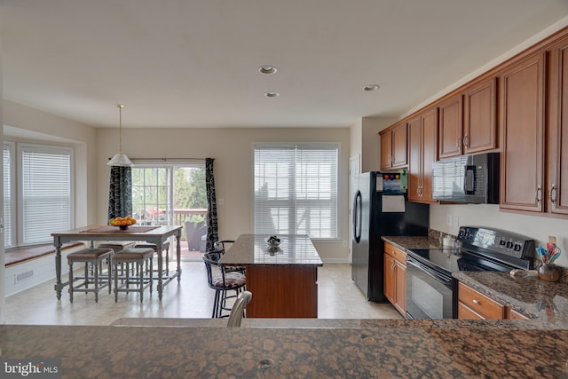 kitchen featuring recessed lighting, a breakfast bar, brown cabinetry, black appliances, and a center island