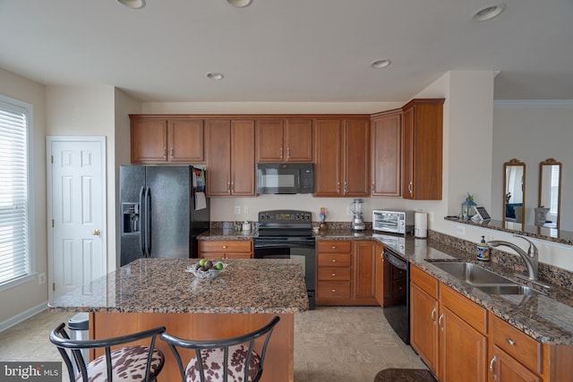 kitchen with dark stone counters, a breakfast bar area, brown cabinetry, black appliances, and a sink