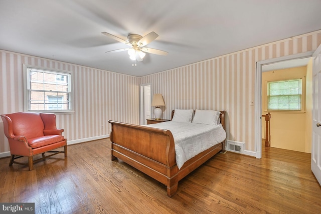 bedroom with wallpapered walls, wood finished floors, baseboards, and ceiling fan