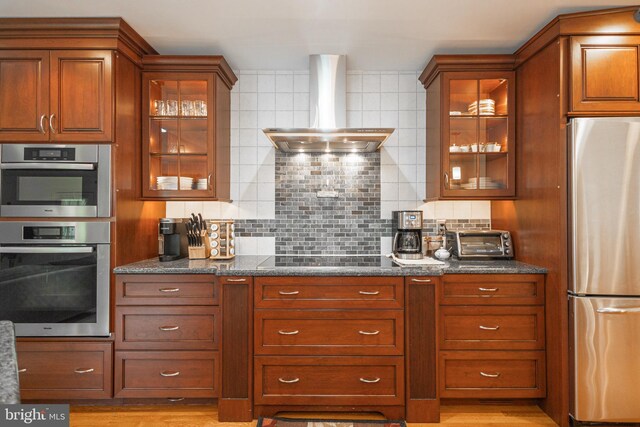 kitchen with tasteful backsplash, dark stone countertops, a toaster, wall chimney exhaust hood, and appliances with stainless steel finishes
