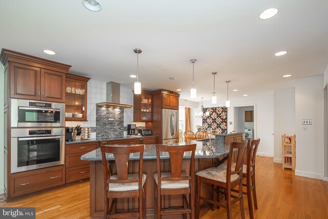 kitchen with wall chimney range hood, a kitchen breakfast bar, a spacious island, backsplash, and appliances with stainless steel finishes