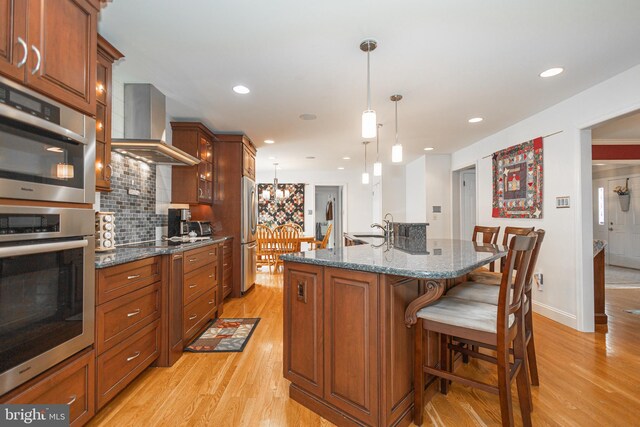 kitchen with wall chimney exhaust hood, stainless steel appliances, light wood-style flooring, a kitchen breakfast bar, and a sink