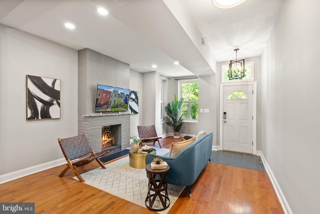 living area featuring baseboards, visible vents, a chandelier, a brick fireplace, and hardwood / wood-style floors