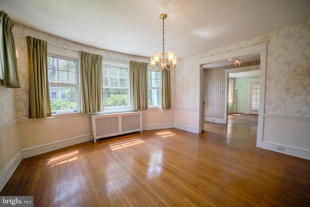 unfurnished dining area featuring wallpapered walls, an inviting chandelier, radiator heating unit, and hardwood / wood-style floors