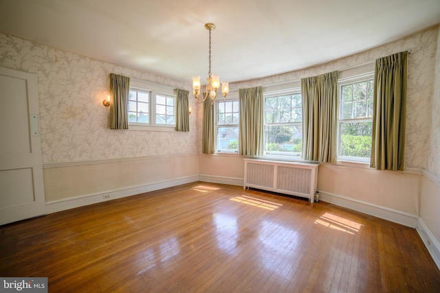 unfurnished dining area featuring wood-type flooring, radiator heating unit, a healthy amount of sunlight, and an inviting chandelier