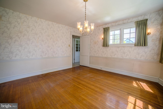 unfurnished dining area with a notable chandelier, hardwood / wood-style flooring, and a wainscoted wall
