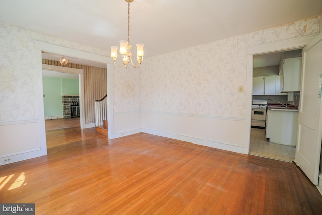 unfurnished dining area with a sink, wallpapered walls, light wood finished floors, and a notable chandelier