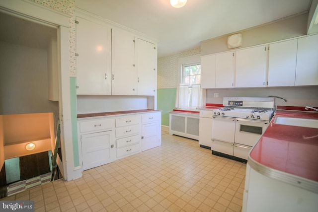 kitchen with white cabinets, wallpapered walls, double oven range, and a sink