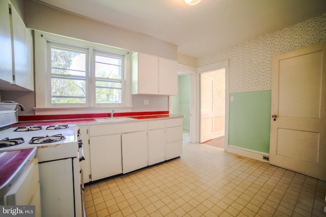 kitchen featuring a sink, stove, white cabinets, and wallpapered walls