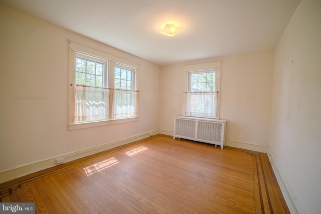 spare room with radiator heating unit, baseboards, and wood finished floors