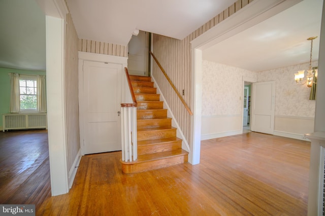 staircase featuring wainscoting, wood finished floors, radiator heating unit, wallpapered walls, and a chandelier