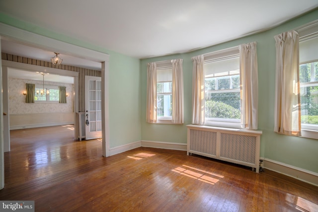 unfurnished room featuring radiator heating unit, baseboards, wood-type flooring, and a healthy amount of sunlight
