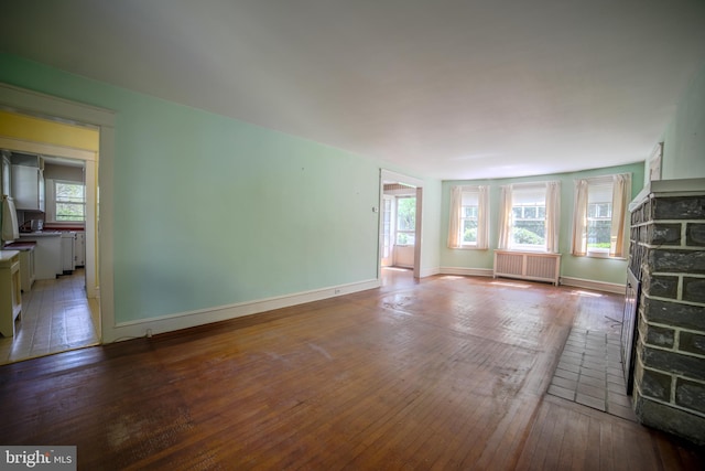 unfurnished living room with wood-type flooring, baseboards, and radiator heating unit