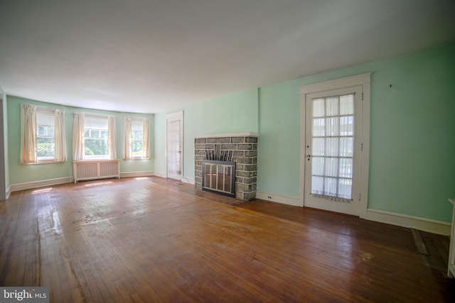 unfurnished living room featuring a stone fireplace, a healthy amount of sunlight, radiator heating unit, and hardwood / wood-style floors