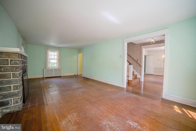 unfurnished living room featuring a brick fireplace, radiator heating unit, hardwood / wood-style floors, stairs, and baseboards
