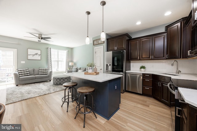 kitchen with a sink, light wood finished floors, stainless steel appliances, open floor plan, and a ceiling fan