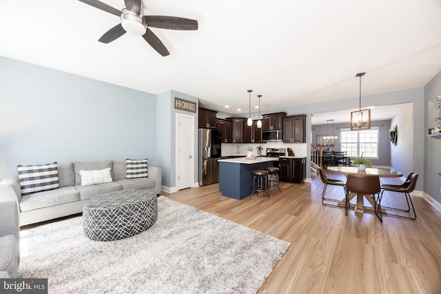 living room featuring baseboards, recessed lighting, light wood finished floors, and ceiling fan with notable chandelier