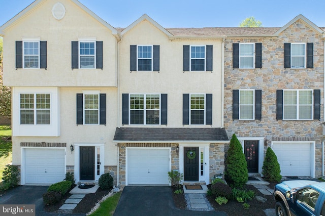 townhome / multi-family property featuring an attached garage, driveway, stone siding, and stucco siding