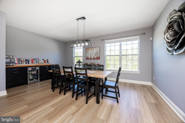 dining room featuring beverage cooler, a dry bar, light wood-style floors, and baseboards