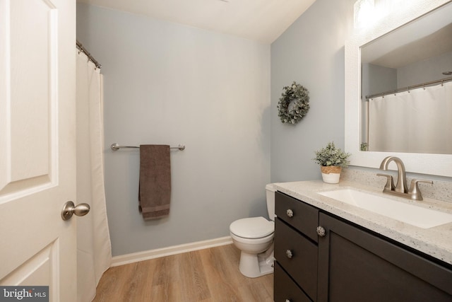 bathroom featuring vanity, baseboards, wood finished floors, and toilet
