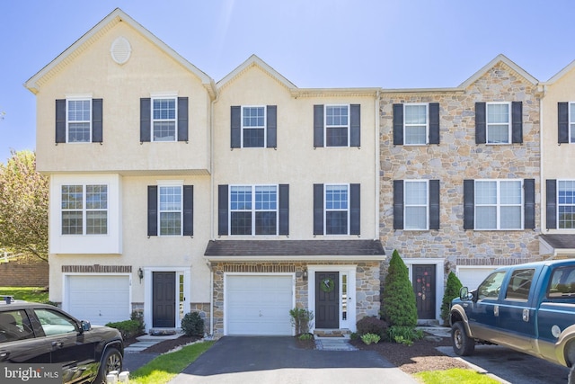 view of property with stucco siding, an attached garage, stone siding, and aphalt driveway
