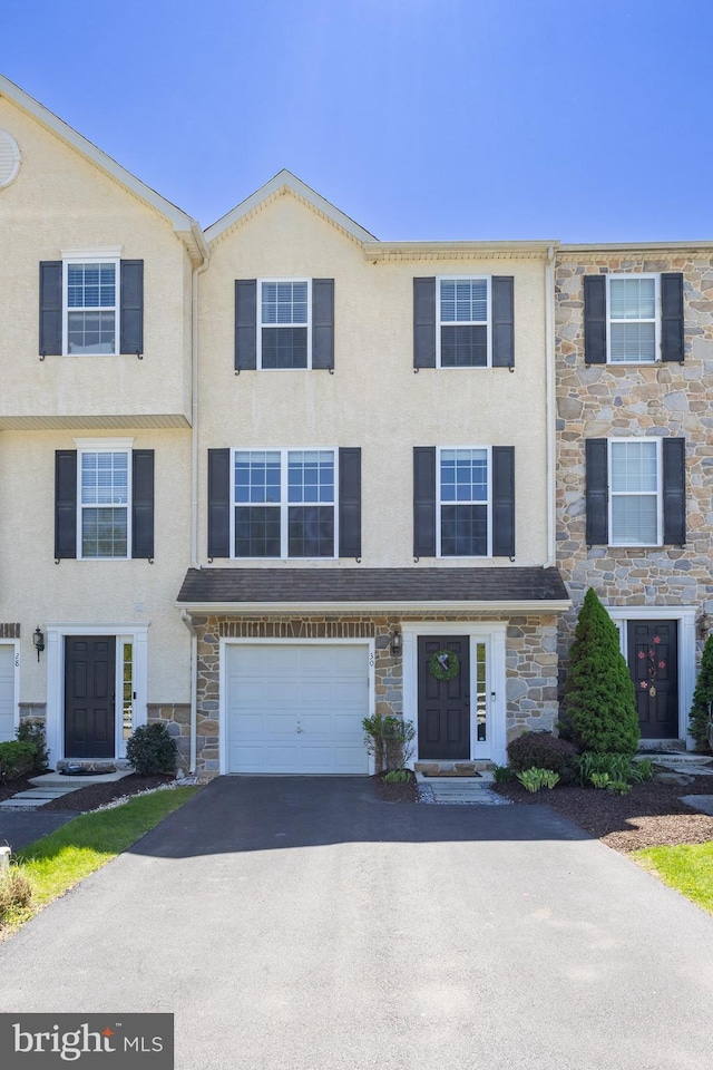 townhome / multi-family property featuring driveway, stone siding, and stucco siding