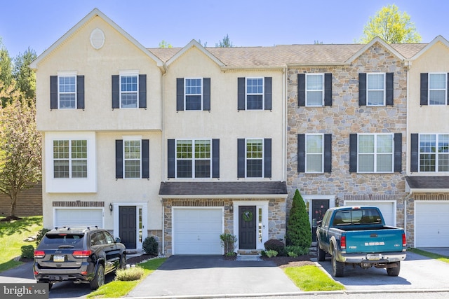 townhome / multi-family property with a garage, stucco siding, driveway, and stone siding