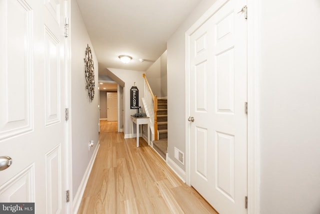 hall with light wood-type flooring, baseboards, visible vents, and stairway