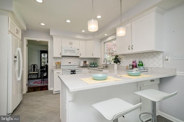 kitchen featuring a peninsula, white appliances, light countertops, white cabinetry, and a sink