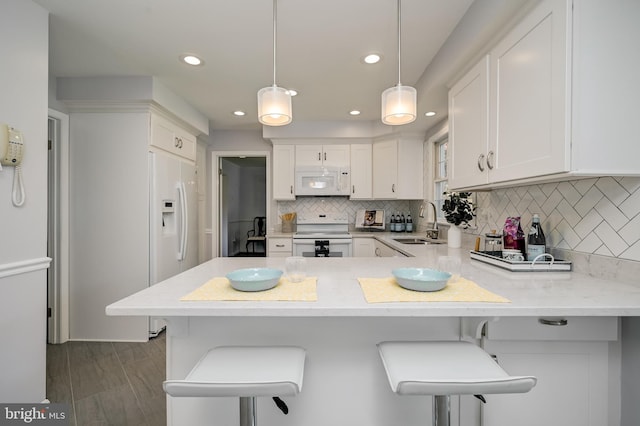 kitchen featuring a sink, white appliances, a peninsula, white cabinetry, and backsplash