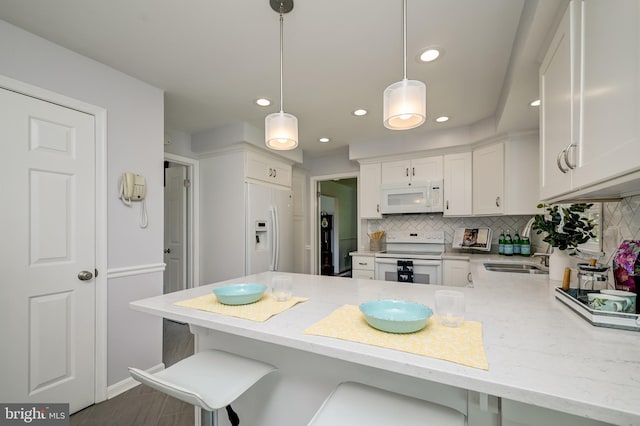 kitchen featuring decorative backsplash, a peninsula, white appliances, a kitchen breakfast bar, and white cabinets