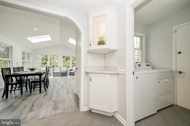 interior space featuring a wealth of natural light, washer and clothes dryer, lofted ceiling with skylight, and light wood-type flooring