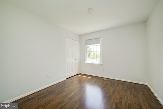 empty room featuring baseboards, dark wood-style flooring, and visible vents
