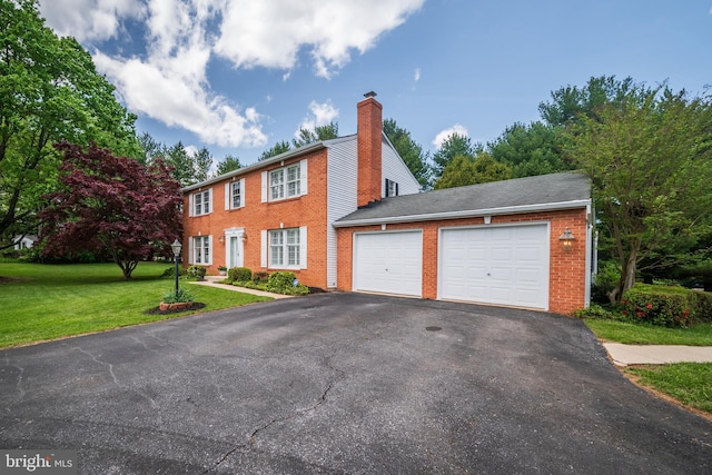 colonial-style house featuring a garage, aphalt driveway, a front yard, a chimney, and brick siding