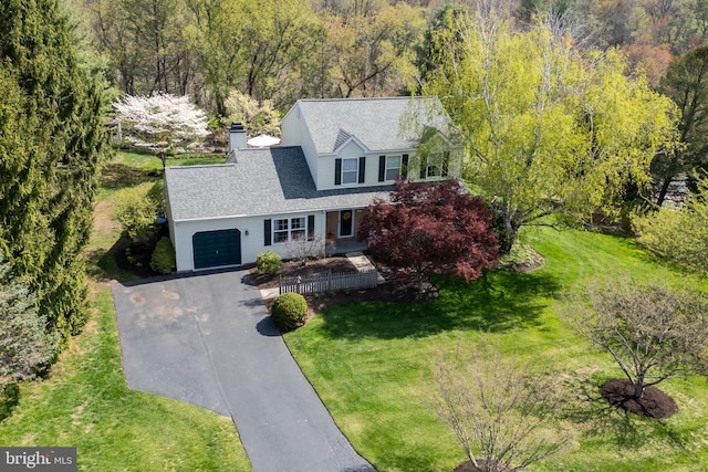 new england style home featuring a garage, a chimney, driveway, and a front yard