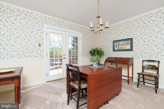 carpeted dining space featuring wallpapered walls, a wainscoted wall, a notable chandelier, french doors, and crown molding