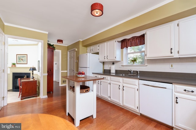 kitchen featuring dark countertops, white appliances, crown molding, and a sink