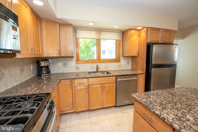 kitchen with a sink, dark stone counters, backsplash, and stainless steel appliances
