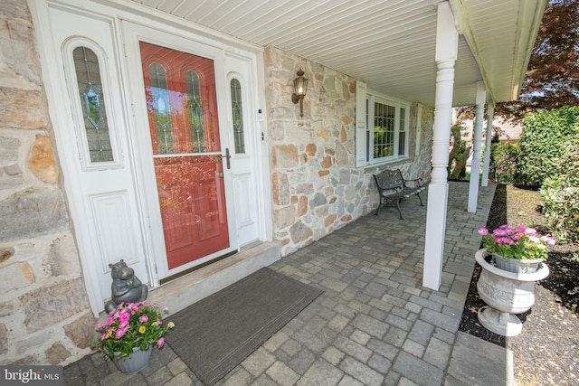 doorway to property featuring a porch and stone siding