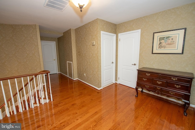 empty room featuring wallpapered walls, visible vents, and wood finished floors