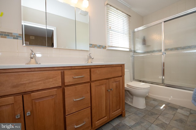 full bathroom with double vanity, a sink, bath / shower combo with glass door, tile patterned floors, and toilet