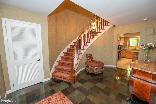 stairway with baseboards, wallpapered walls, and a notable chandelier