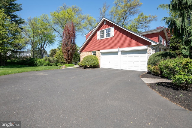 view of side of property with driveway, stone siding, and a garage